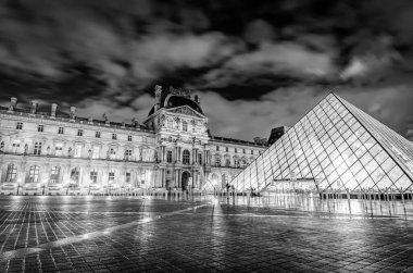Gece Paris 'teki Louvre Müzesi' nin dramatik siyah beyaz görüntüsü. Etrafta çok az turist var. Fransa 'yı gezmek. Gökyüzünün kasıtlı olarak bulanıklaşması..
