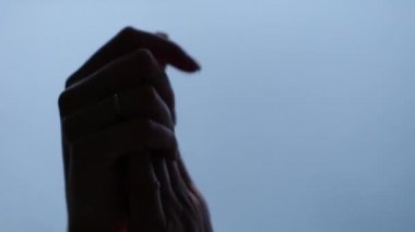 Karı ve kocanın elleri mavi su arka planında birbirine dokunup tutunuyor. Düğün günü karı ve kocanın ellerinin yakın çekimi.