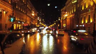 Gece şehir sokağında yağmur yağarken ışıklar ve ulaşım gideriliyor.
