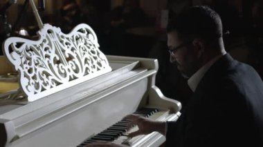 Bir piyanist, seyirci arka planında kendi müziğini icra eder.