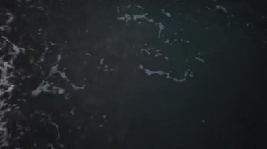 Deniz gelgiti taştan kıyı arka planında kapanıyor. Deniz yüzeyi gün batımında kapanır, alçak açı görünümü