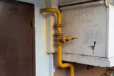 Balkonun yanındaki boruda eski sarı gaz vanası ve kahverengi çelik kapı. Tedarik sistemi yakıt dağıtımı ve gerekirse kapatma izni verdi. Flanşlı ve dirsekli boru hattı. Yatay yönelim.