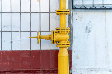Balkonun yanındaki boruda büyük sarı gaz vanası ve fayanslı duvar. Borudaki çarkıfelekli vana, gerekirse gaz dağıtımını ve kapatılmasını sağlıyor. Dikey boru üzerinde flanşörler ve indirgeyiciler.