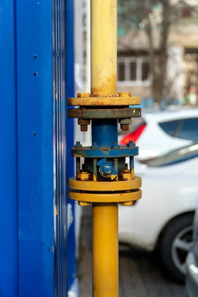 Blue gas crane with flanges on the pipe near dark blue metal wall. Gas supply system is distributed gas and turn it off if necessary, located in the yard. Pipe painted yellow. Vertical orientation.