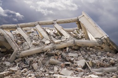 Endüstriyel beton bina deprem tarafından tahrip edildi. Enkaz, toz ve yıkılmış binalarla dolu felaket sahnesi.