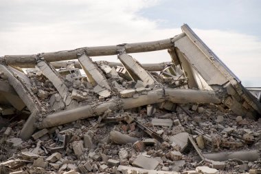 Endüstriyel beton bina deprem tarafından tahrip edildi. Enkaz, toz ve yıkılmış binalarla dolu felaket sahnesi.