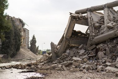 Endüstriyel beton bina deprem tarafından tahrip edildi. Enkaz, toz ve yıkılmış binalarla dolu felaket sahnesi.
