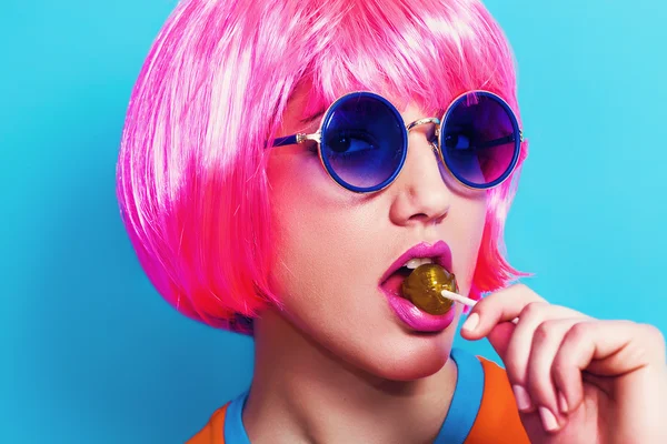 Chica pop con peluca rosa y gafas de sol mientras come piruleta —  Fotos de Stock