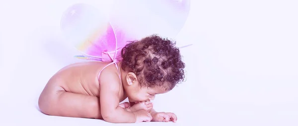 Lovely baby girl tasting her foot while wearing wings letterbox — Stock Photo, Image