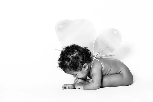 Adorável bebê menina degustação seu pé enquanto vestindo asas monocromático — Fotografia de Stock