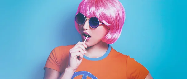 Поп-девушка в парике и солнцезащитных очках и ест леденцы — стоковое фото