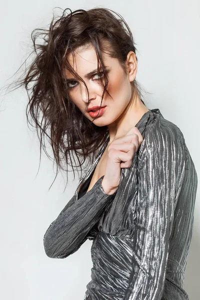 Gorgeous woman portrait with messy hair posing while wearing silver dress