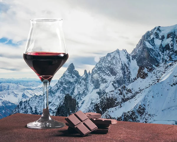 Bicchiere di vino rosso con cioccolato e bellissimo paesaggio montano innevato — Foto Stock