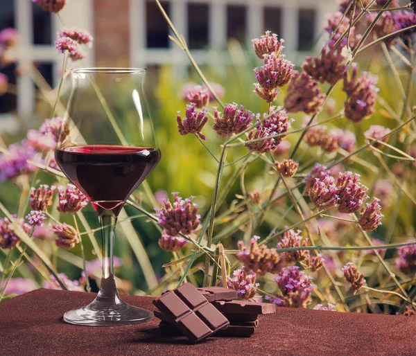 Ποτήρι κόκκινου κρασιού τύπου με σοκολάτα και τα όμορφα ροζ λουλούδια — Φωτογραφία Αρχείου