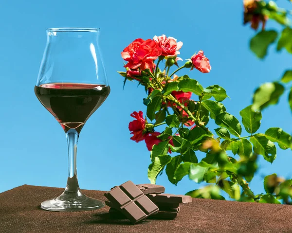 Bicchiere di vino con cioccolato e belle rose rosse con cielo blu — Foto Stock