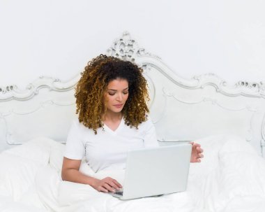 Güzel kız portre cov altında yatakta otururken dizüstü bilgisayar kullanarak