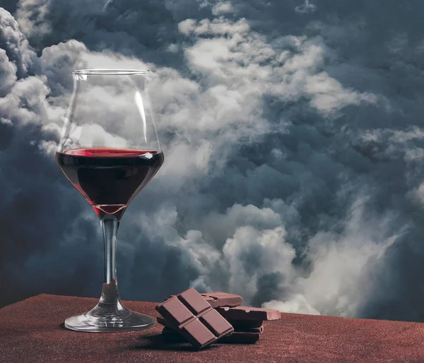 Bicchiere di vino rosso con cioccolato e bellissimo paesaggio nuvoloso tempestoso — Foto Stock