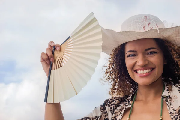 Mujer hermosa y feliz sonriendo y sosteniendo ventilador en verano caliente — Foto de Stock