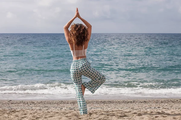 Schöne Frau mit lockigem Haar beim Yoga am Strand — Stockfoto