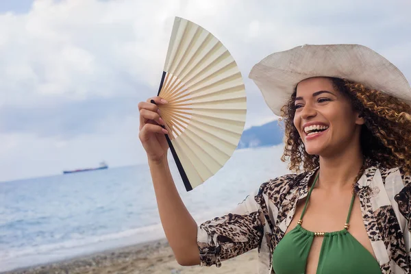 Felice giovane donna sorridente e tenendo ventilatore sulla spiaggia — Foto Stock