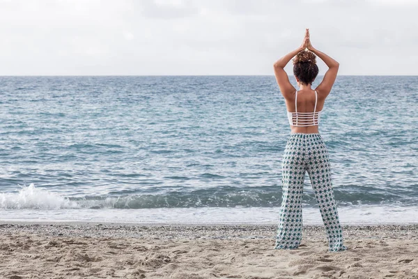 年轻女子看着大海和沙滩上练瑜伽 — 图库照片