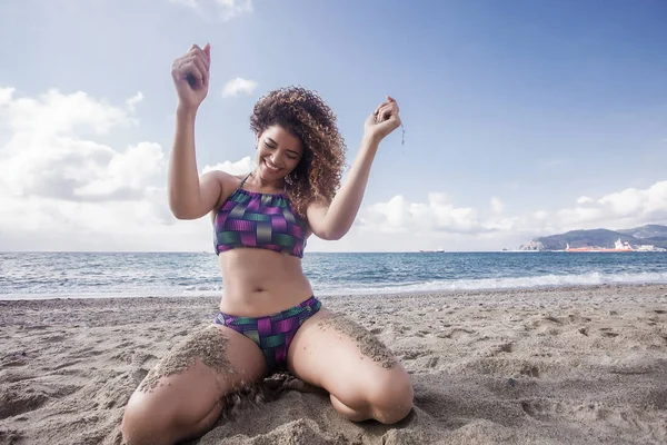 Mujer feliz retrato jugando con la arena mientras se arrodilla en la playa — Foto de Stock