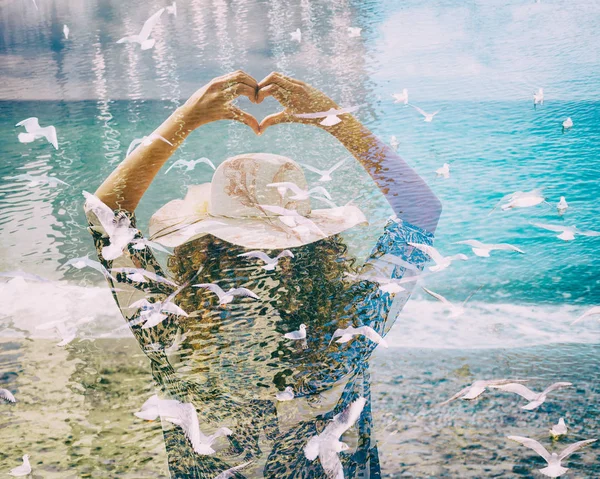 Doble exposición de la mujer haciendo gesto en forma de corazón y gaviotas volando — Foto de Stock