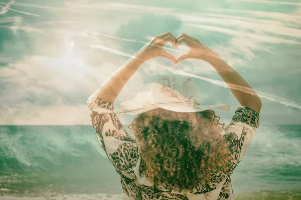 Doble exposición de la mujer haciendo gesto en forma de corazón con el paisaje marino y el paisaje nublado — Foto de Stock