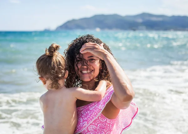 Güzel ve mutlu anne küçük kızı plajda holding