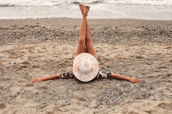 Retrato de mujer usando sombrero y manteniendo las piernas en la playa — Foto de Stock