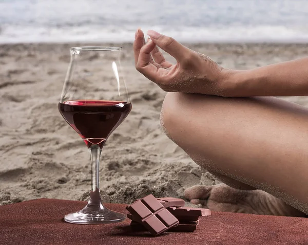 Copo de vinho tinto com chocolate e mulher praticando ioga na praia — Fotografia de Stock