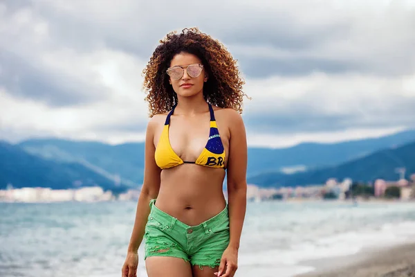 Mujer hermosa y serena caminando por la playa y usando gafas de sol — Foto de Stock