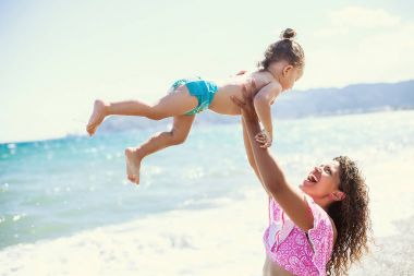 Mutlu anne portre holding ve küçük kızıyla birlikte sahilde oynarken