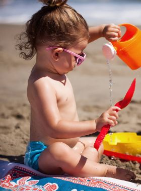 Sahilde oturan ve kumla oynayan küçük kız portre