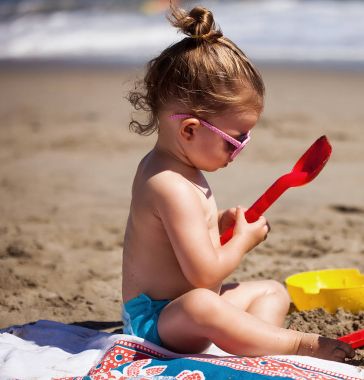 Sahilde oturan ve kumla oynayan küçük kız