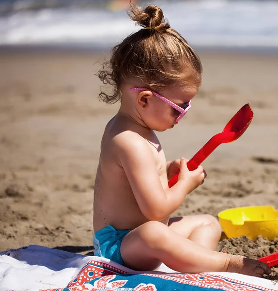 Sahilde oturan ve kumla oynayan küçük kız