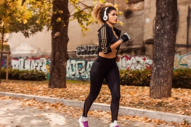 Kulaklık ve sportif giysiler giyen güzel jogger portre kentsel sonbahar Park,
