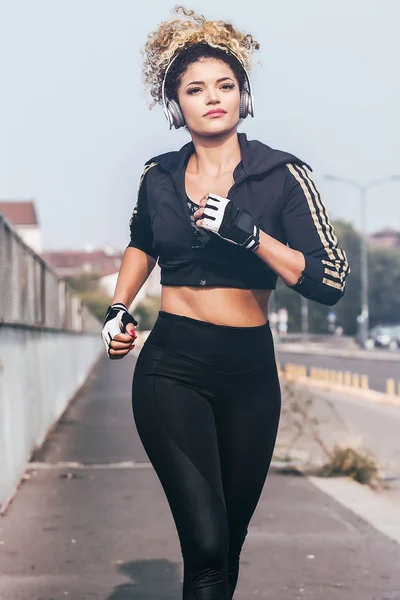 Beautiful jogger portrait running in the city while wearing headphpnes and sporty clothes — Stock Photo, Image