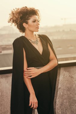 Çatıda güneş ışığı altında duran ve bir kenara bakıyor güzel ve zarif kadın