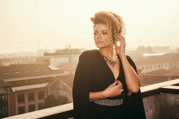 Schönes und nachdenkliches Frauenporträt in elegantem schwarzen Kleid und Blick auf die Stadtlandschaft — Stockfoto