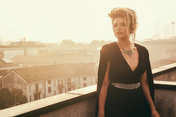 Mujer hermosa y pensativa con elegante vestido negro y mirando el paisaje urbano — Foto de Stock