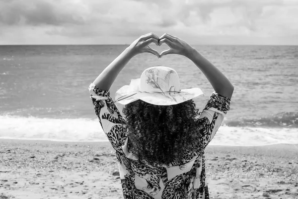Hermosa mujer joven retrato haciendo gesto de corazón en la playa, monocromo — Foto de Stock