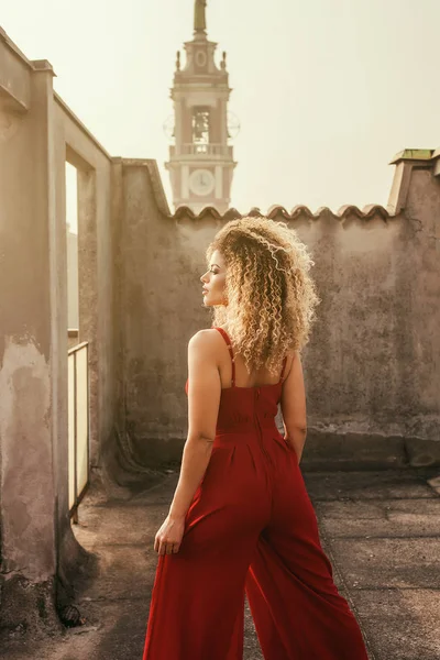 Piękna i elegancka kobieta z powrotem portret stojący na dachu podczas noszenia czerwonej sukience — Zdjęcie stockowe