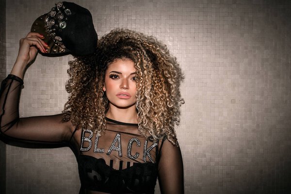 Female gangster portrait with gorgeous hair holding hip hop cap full of pins
