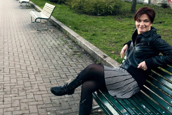 Mooie vrouw portret zittend op de bank terwijl het dragen van leren jas en rok — Stockfoto