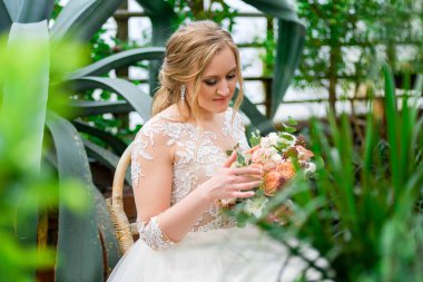 bride in a greenhouse looks at a bouquet