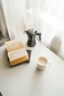 geyser coffee maker, cappuccino and book on a white table