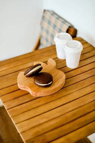 cookies on a wooden stand and 2 cardboard cup with coffee
