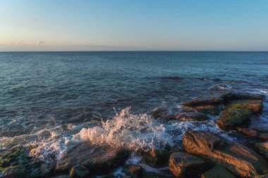 Gün batımında kıyı kayalıklarında dalgalanan dalgalar.