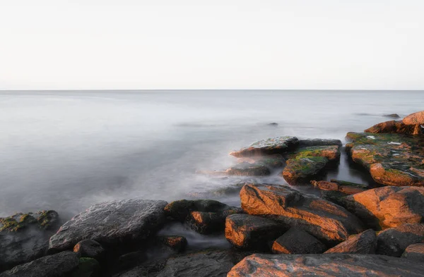 Скалистое море с размытой спокойной водой на восходе солнца — стоковое фото